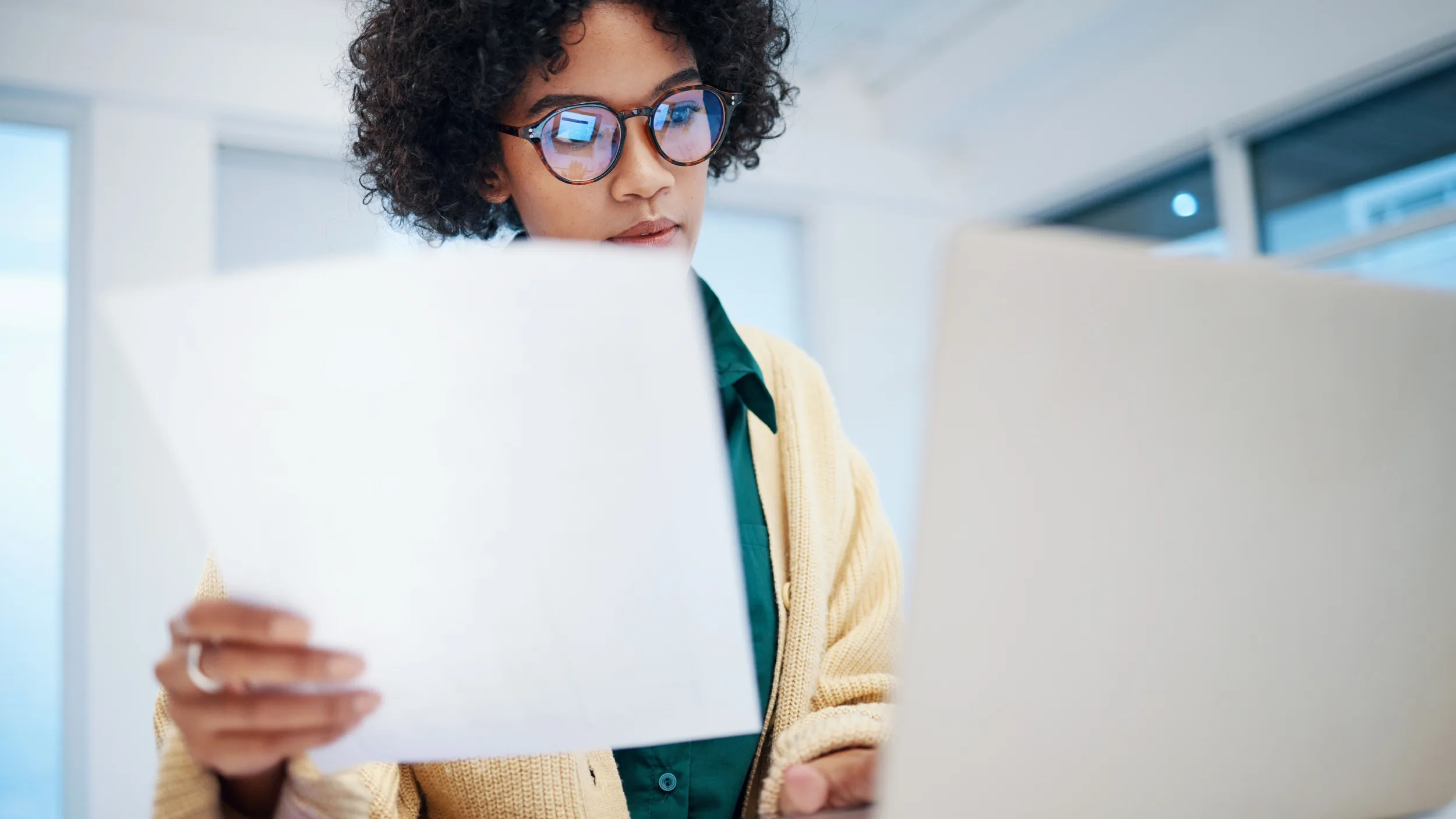 woman holding papers and looking at a computer screen