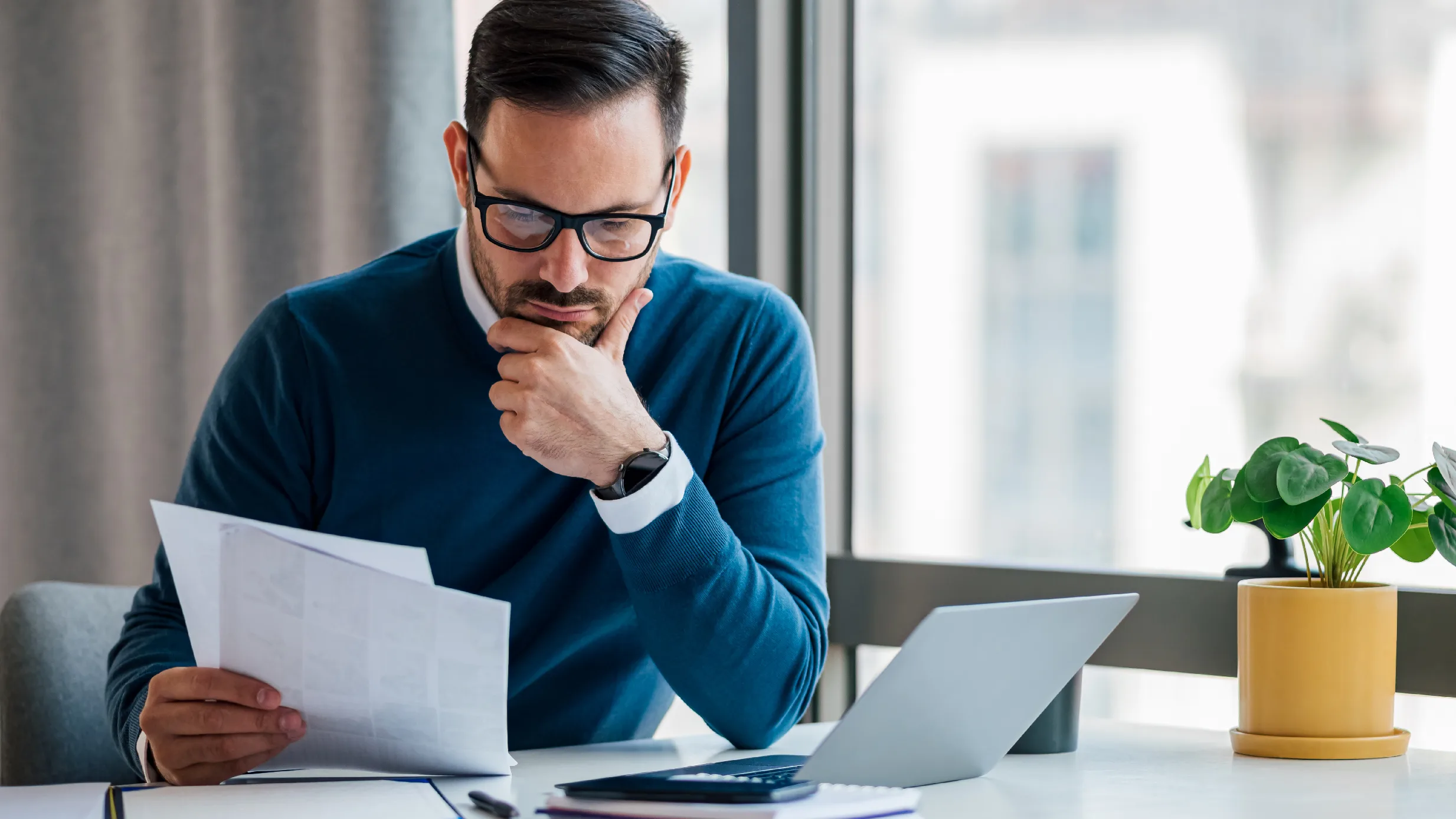 man holding papers and looking at a computer screen