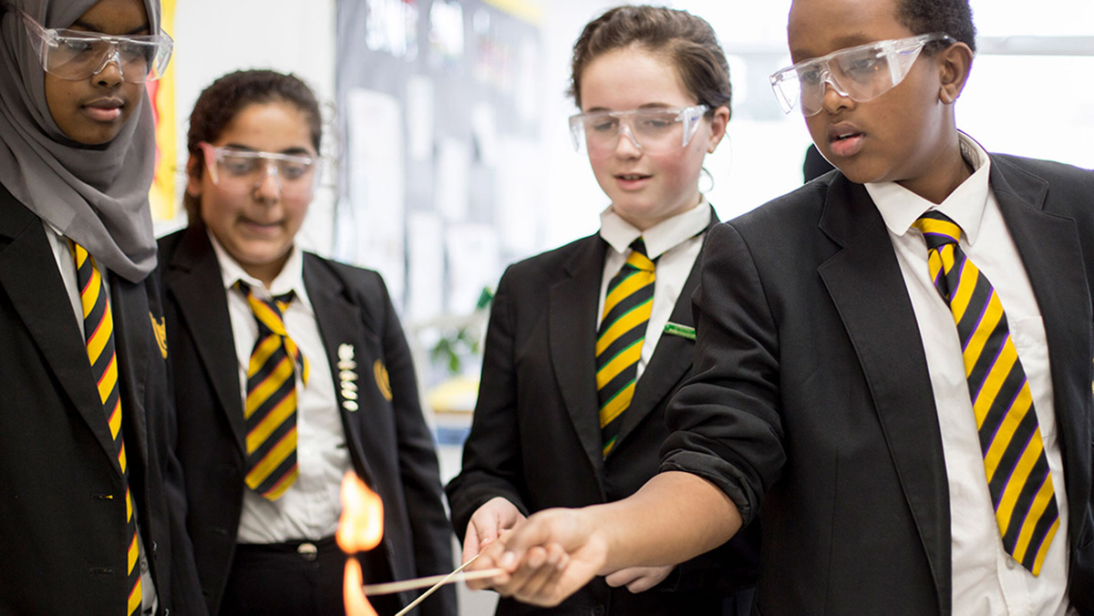 A diverse set of students wearing school uniforms and safety glasses participate in a science experiment at school.