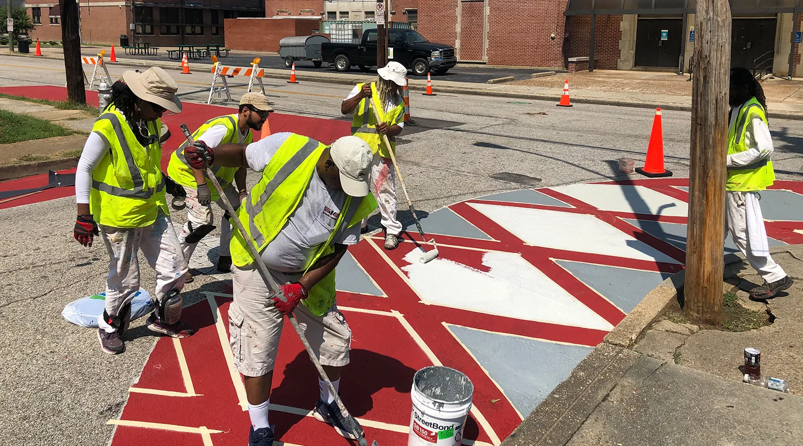 Five people wearing yellow high visibility safety vests painting geometrical shapes on the pavement
