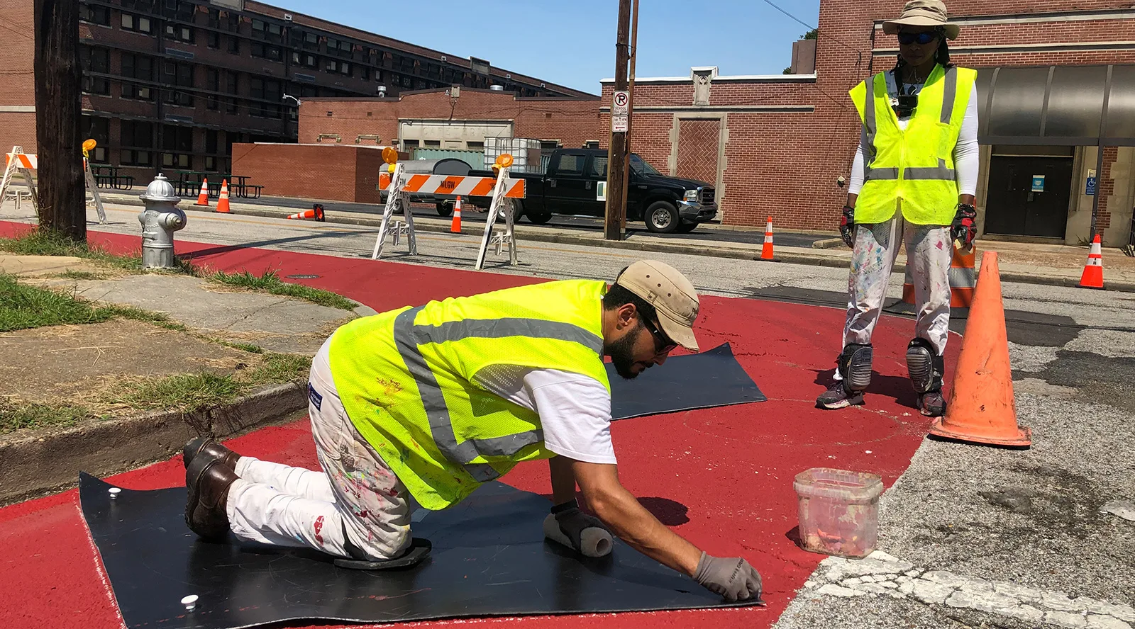 A man and a woman wearing bright yellow vests painting the sidewalk