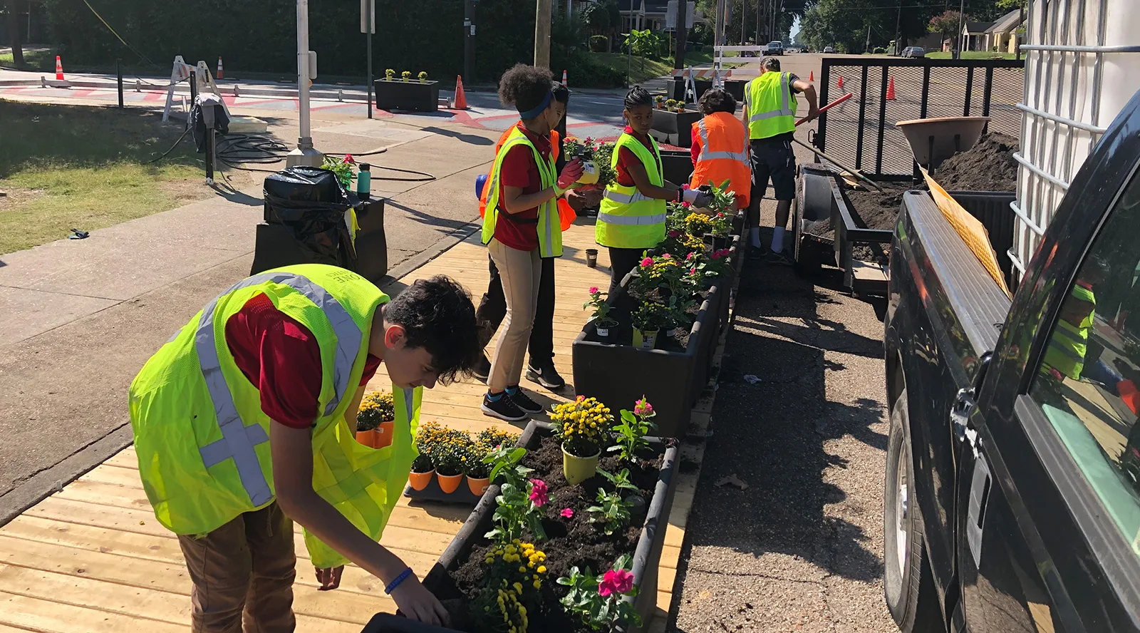 Children & city employees wearing yellow safety vests planting flowers in the sidewalk flower pots