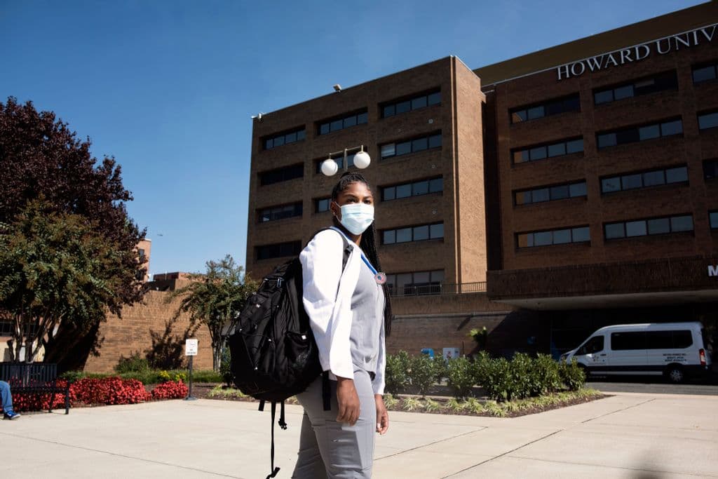 A medicine student standing in front of Howard University College of Medicine with her mask on