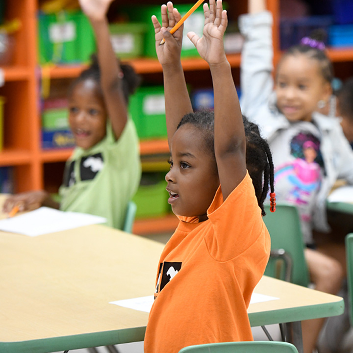 Small kids engage in classroom discussion, raising hands