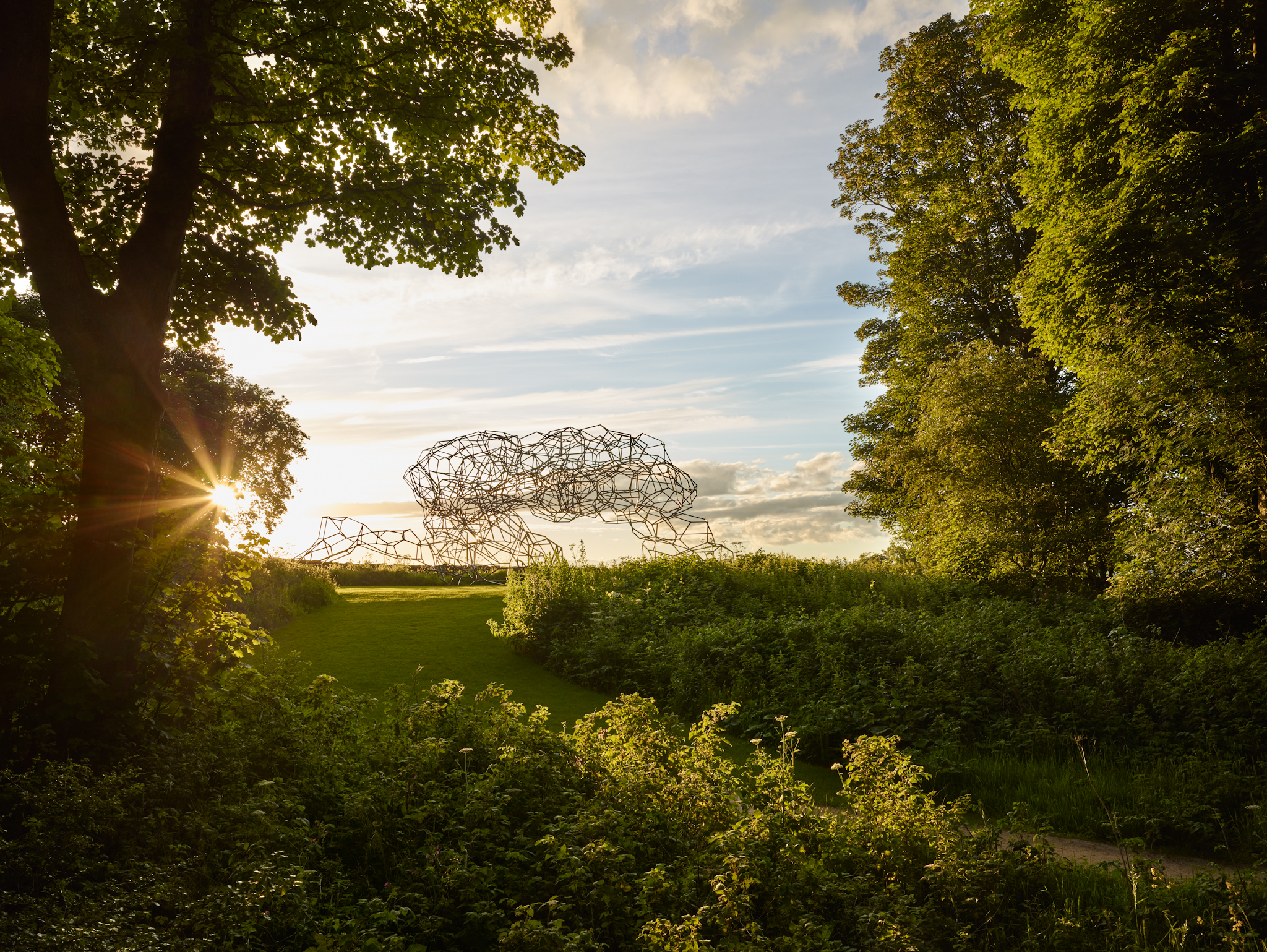 Antony Gormley sculpture in the grounds of Jupiter Artland. Framed by green trees and blue sky.