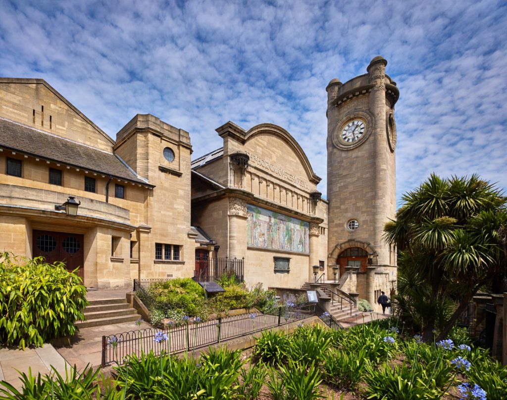 Color photo of the exterior of the Horniman Museum – a yellowstone building with mosaic and clock tower