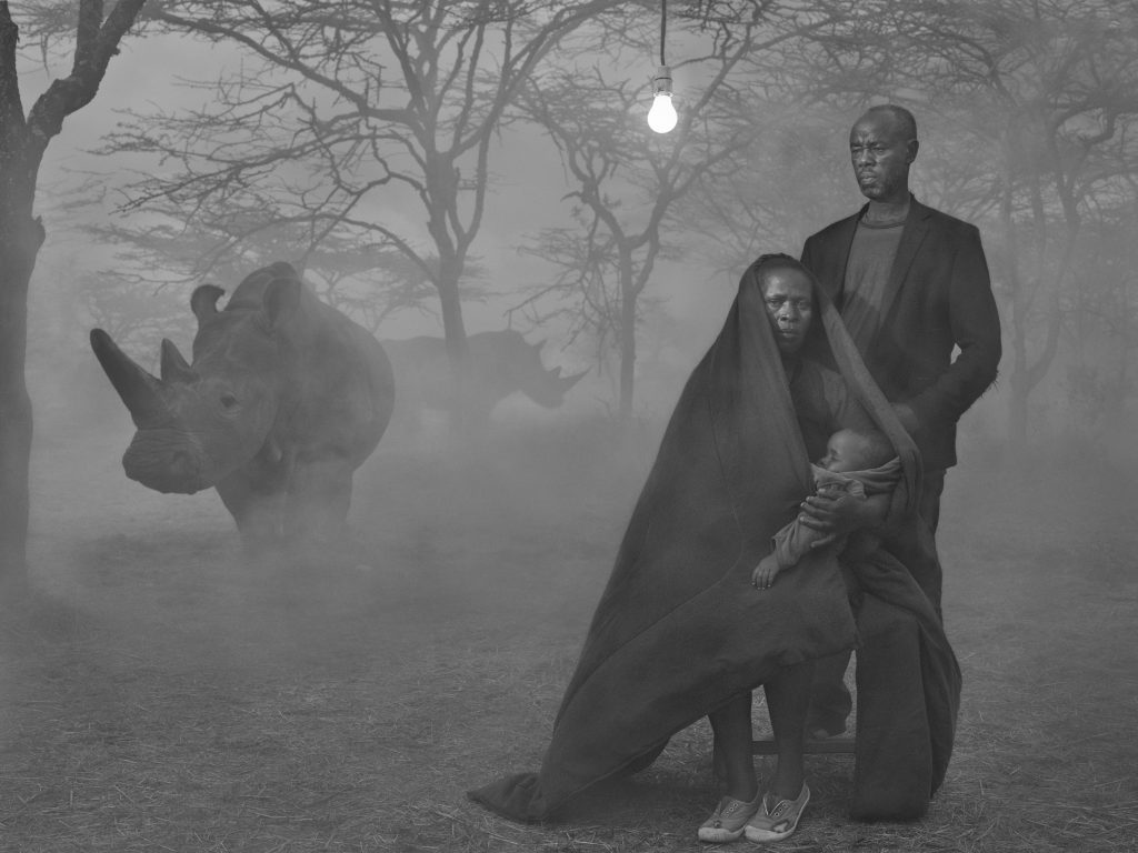 Local couple from Kenya holding a baby with a white rhino in the background in the fog