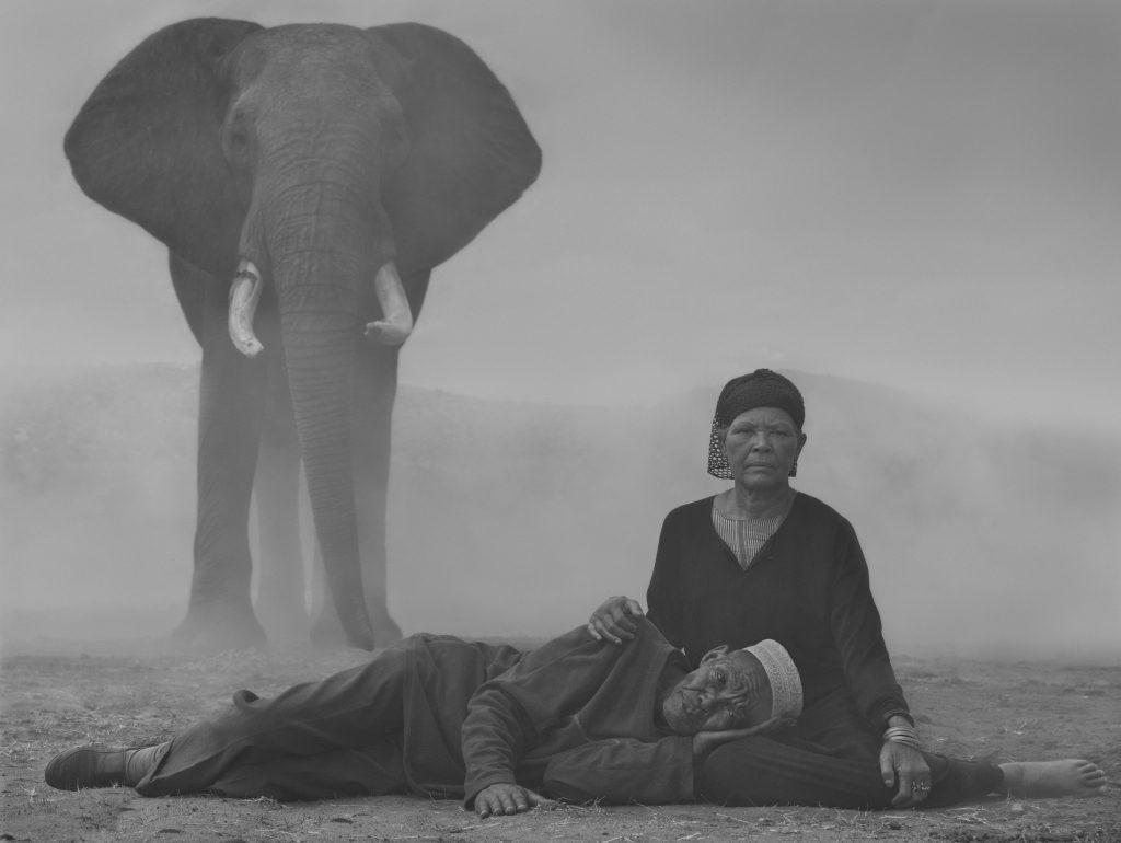 Local Kenyan woman holding men with an elephant in the background in the fog