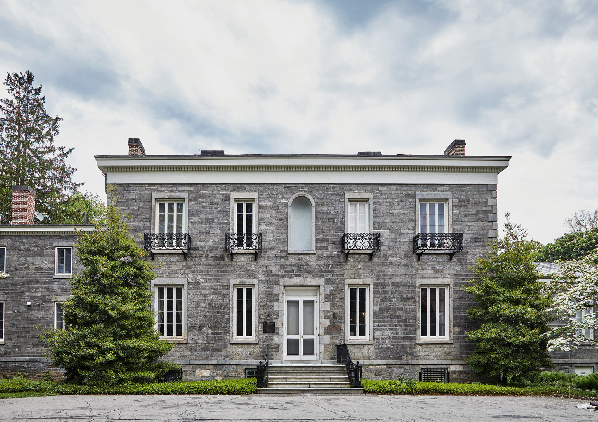 Stone building with two floors, center door, balconies, and two side wings.