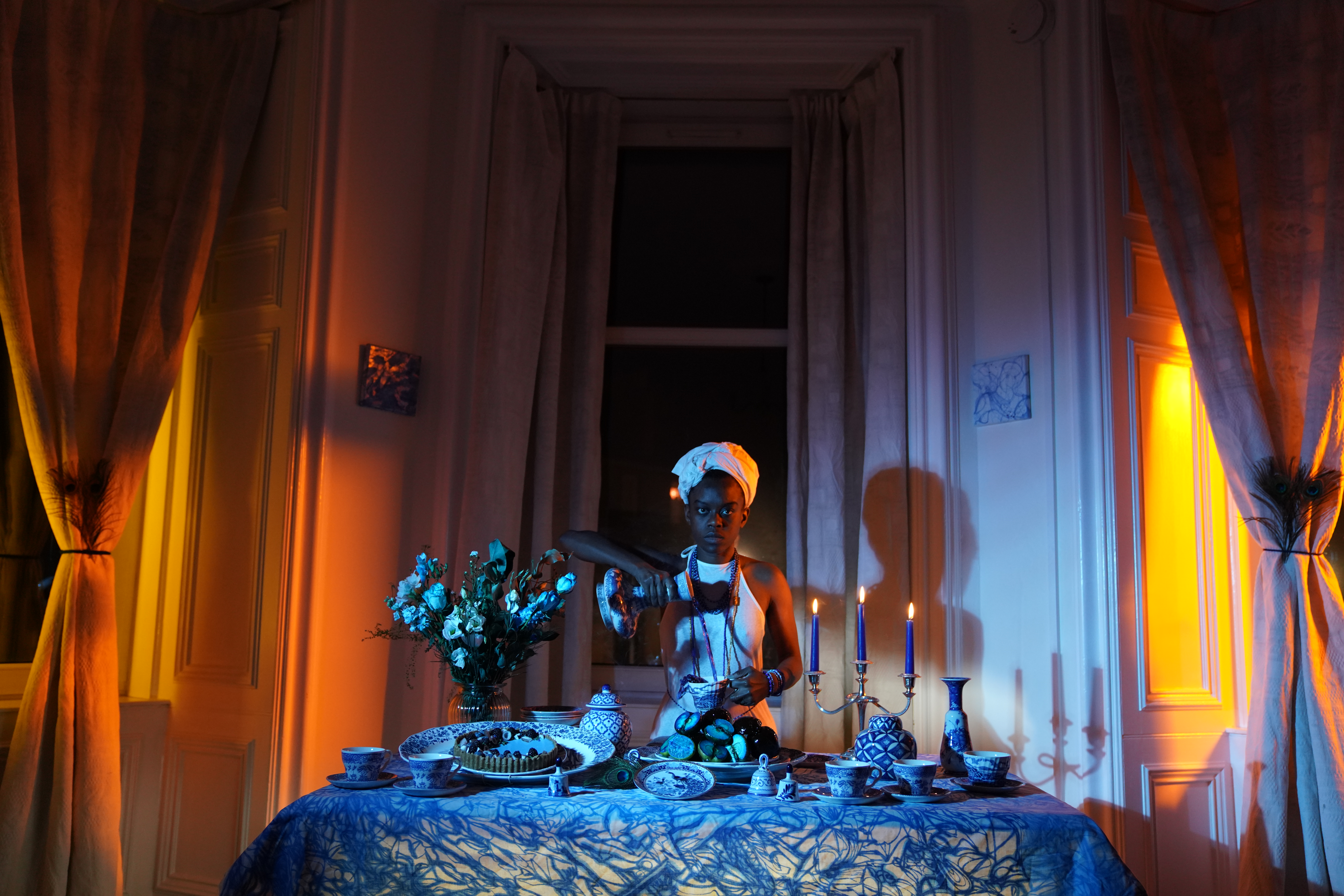 A photograph of a young Black woman pouring blue liquid out of a teapot