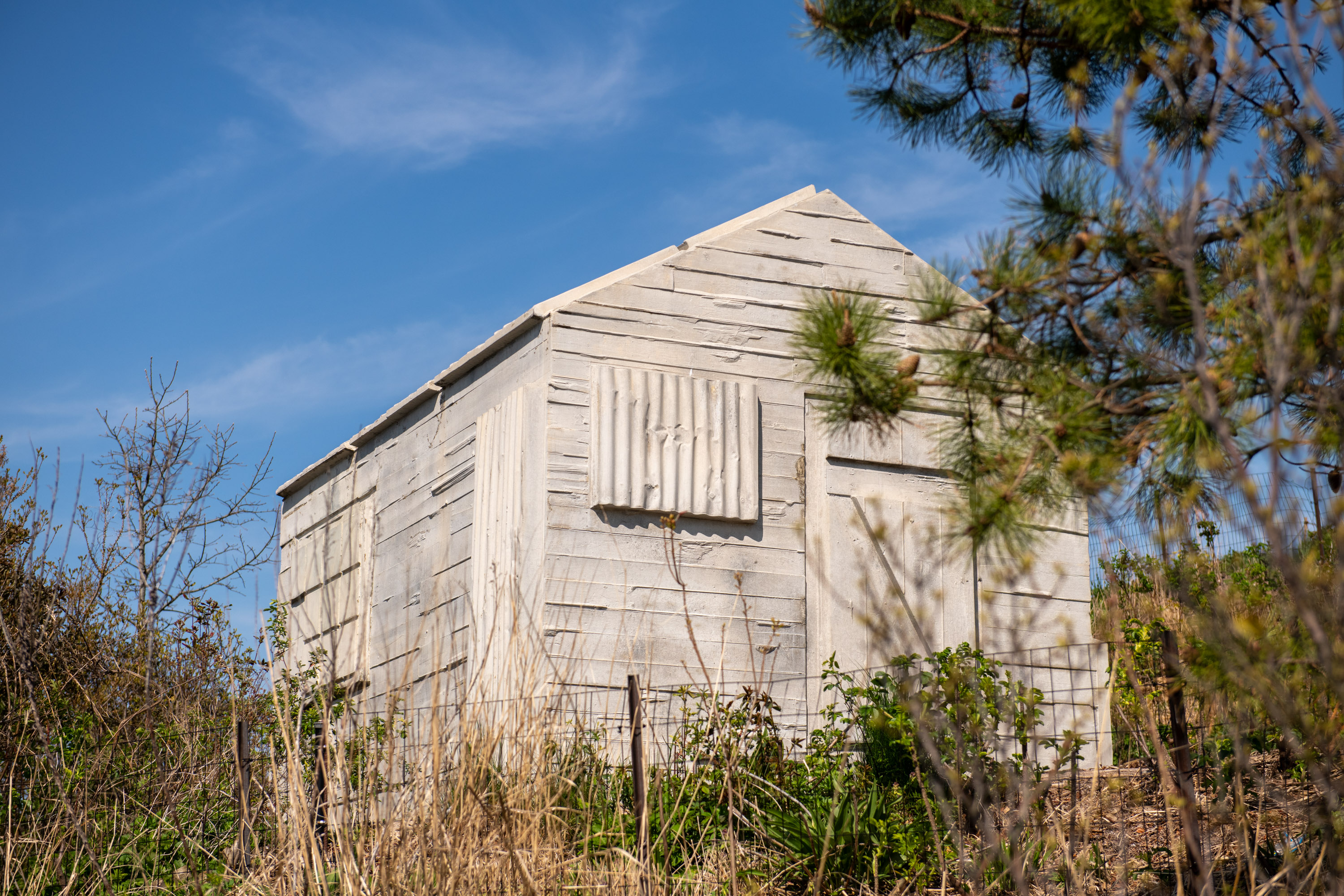 White concrete cast of a cabin surrounded by green and brown foliage.