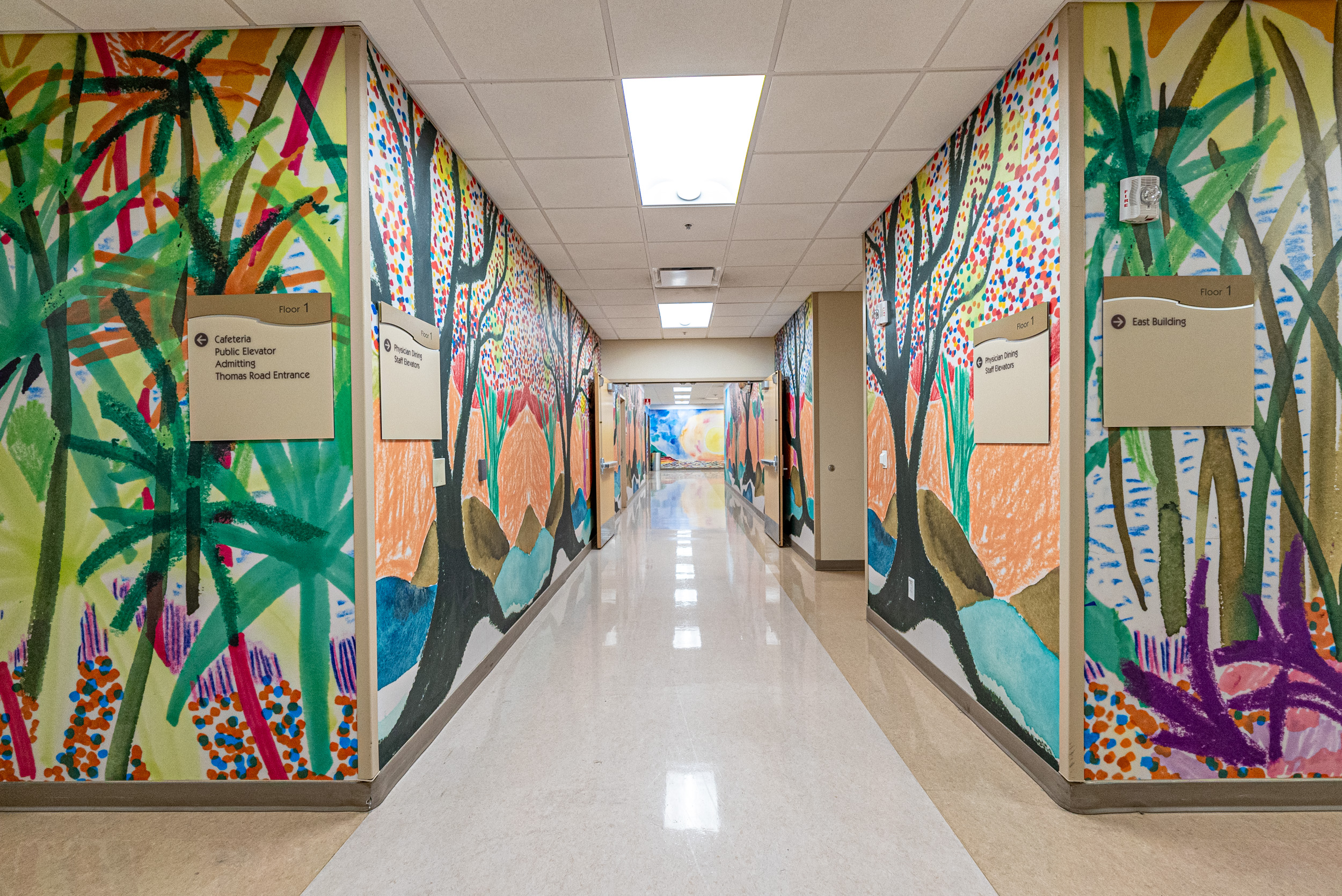 Colorful mural with images of trees lining the walls of a hospital hallway