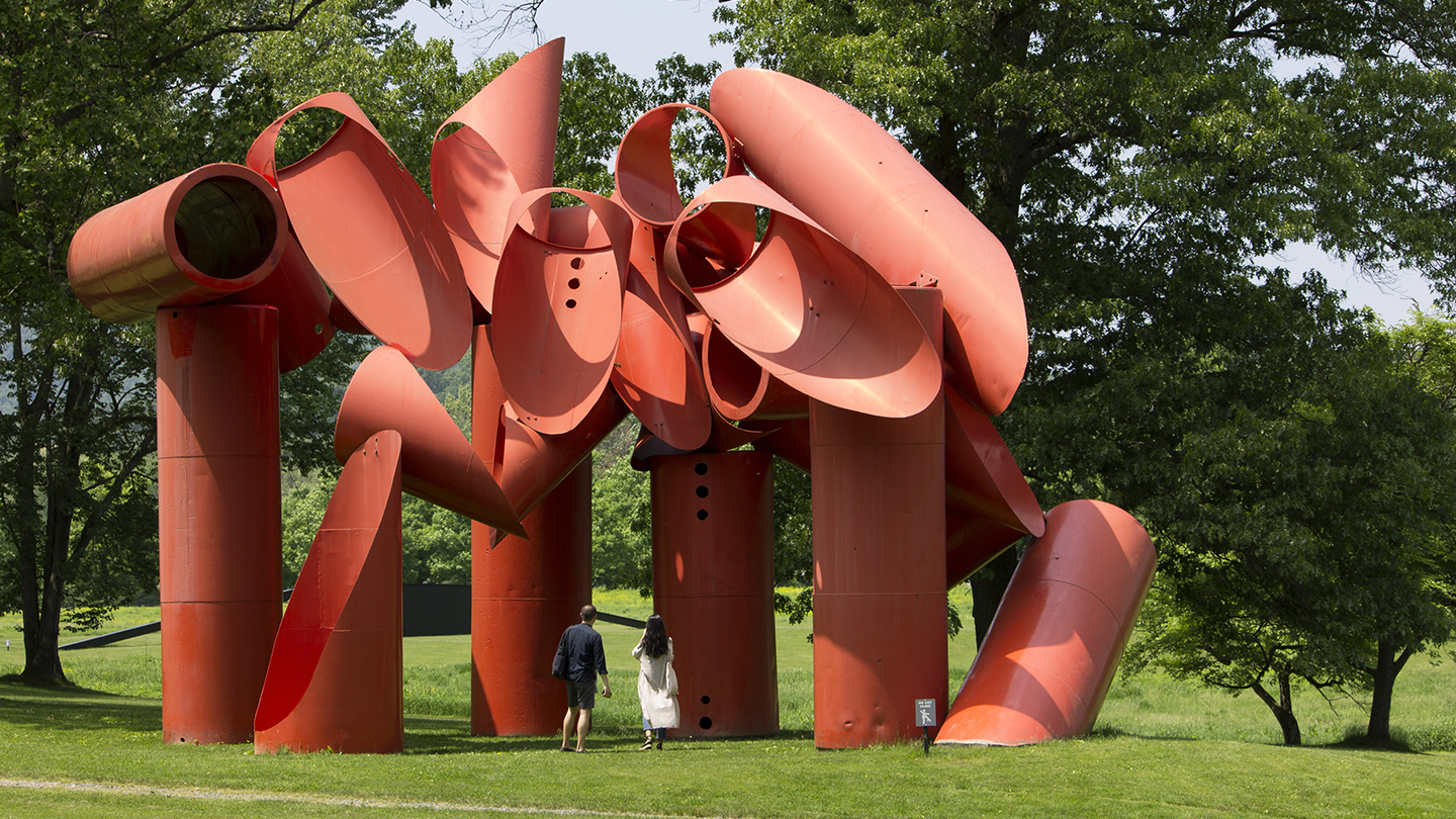 Shiny red cylinders laid on a slant with surrounding trees and shrubbery.