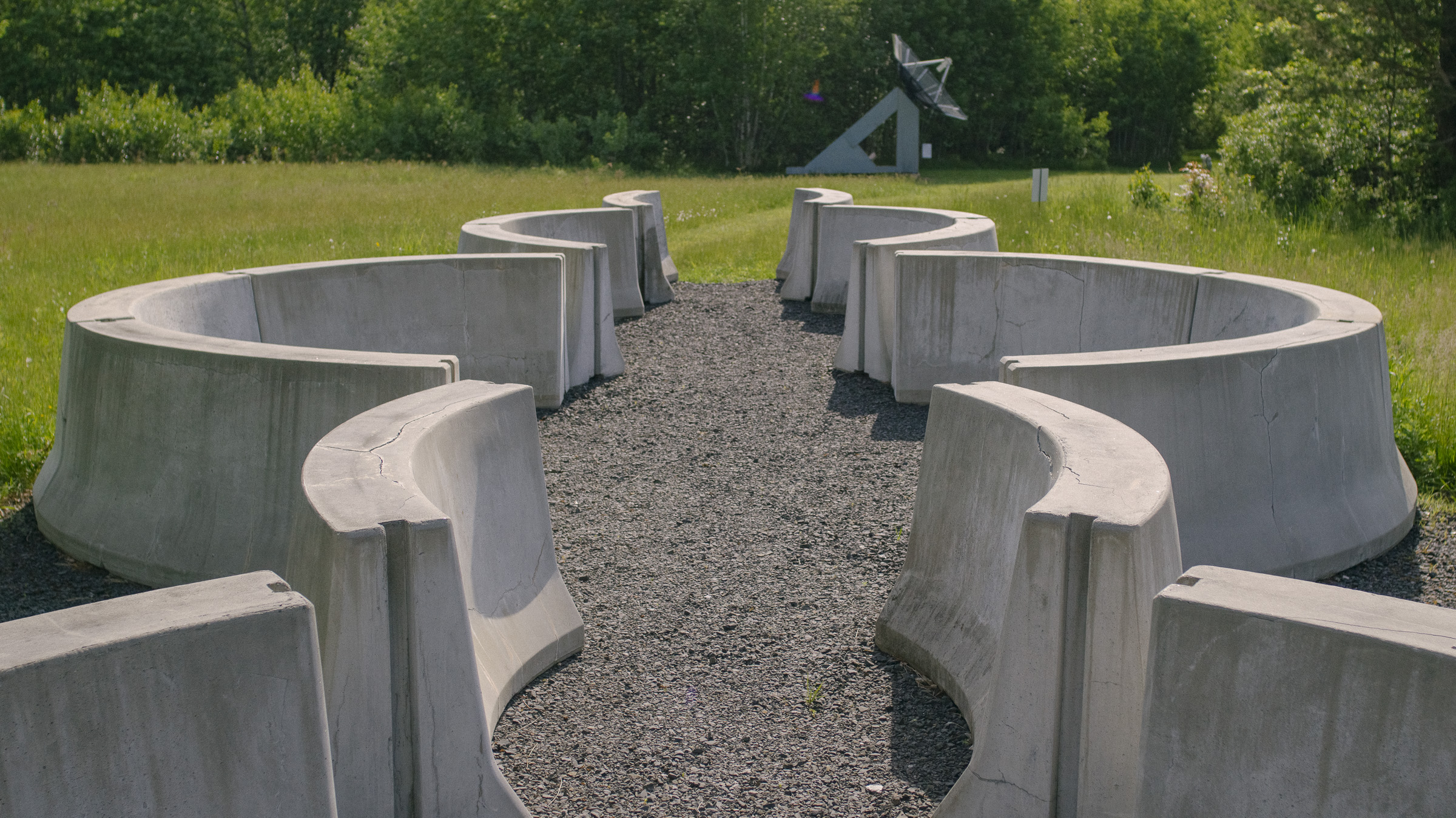 A series of rounded concrete jersey barriers on a gravel surface within a grassy lawn.