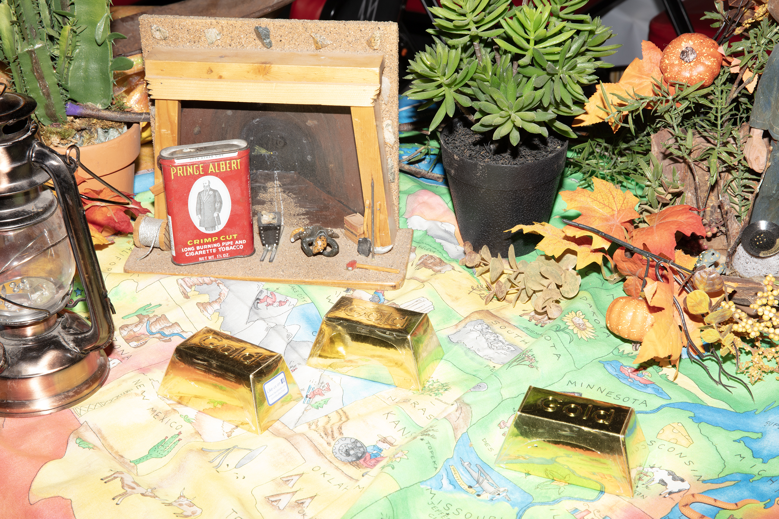 A colour image of a collection of objects scattered across a map laid on a surface. Items include a gas lamp, gold bars and a potted plant among others.