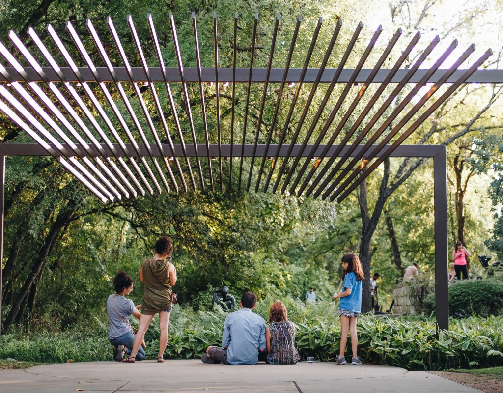 Group of people sitting and standing looking at artwork among foliage.