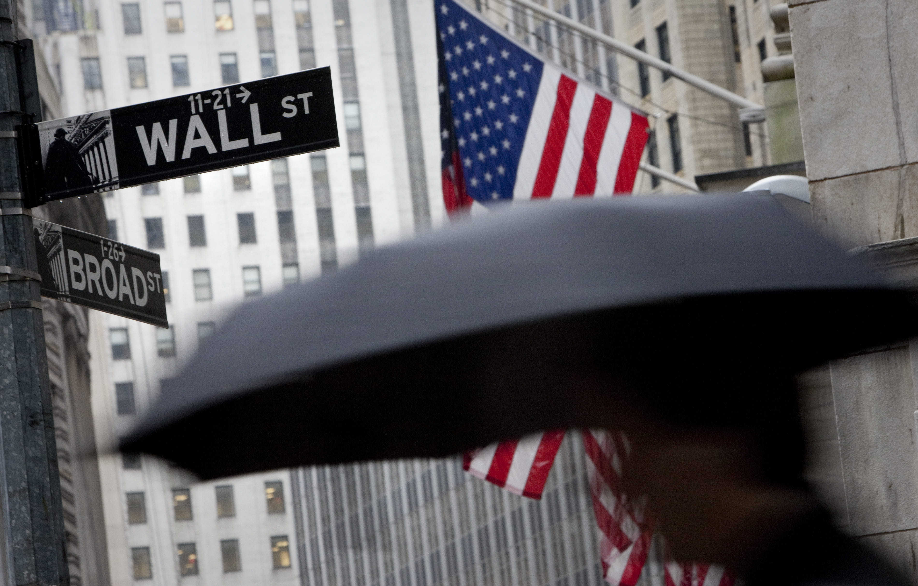 A pedestrian carrying an umbrella passes a U.S. flag on Wall Street in New York