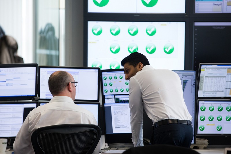 Traders talk whilst examining financial data on computer screens