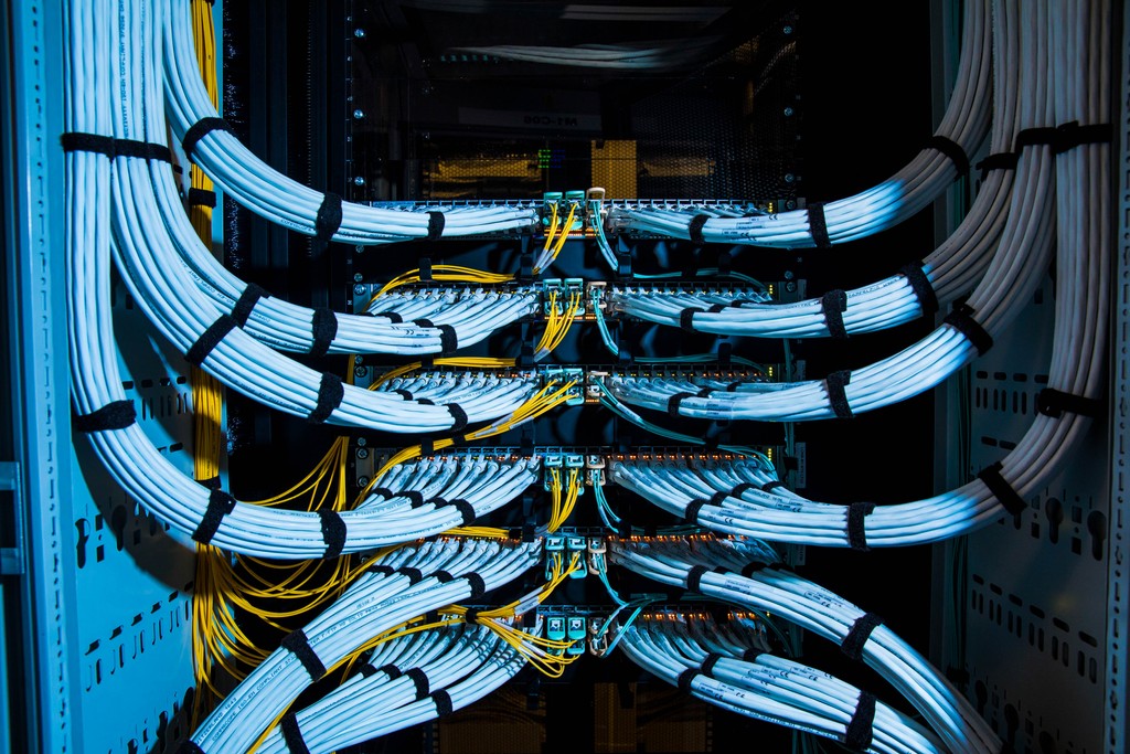 Fiber optic cables, center, and copper Ethernet cables feed into switches inside a communications room