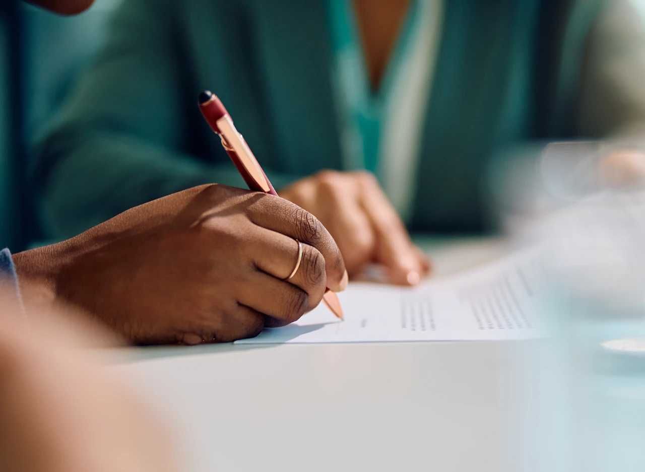 Person holding a pen and signing a document