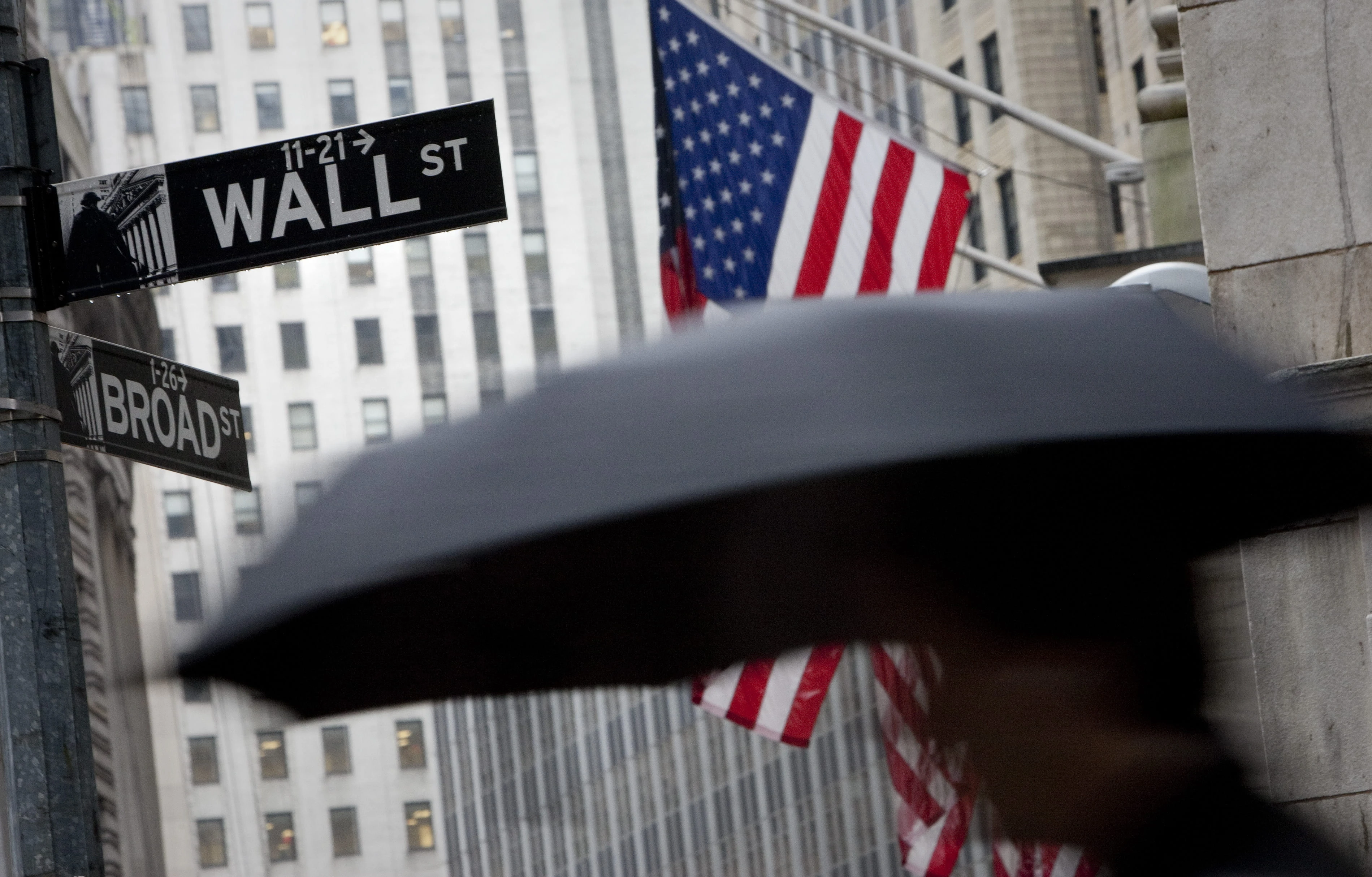 A pedestrian carrying an umbrella passes a U.S. flag on Wall Street in New York