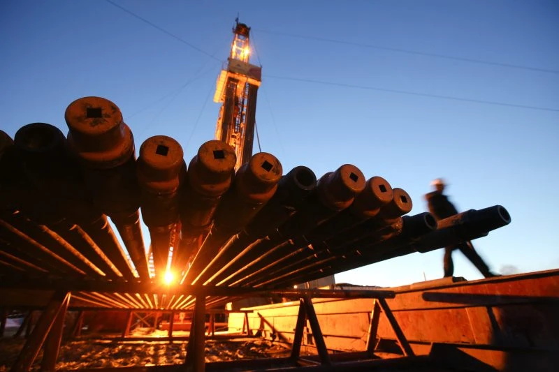 A worker passes an illuminated oil drilling rig and drill pipes in an oilfield