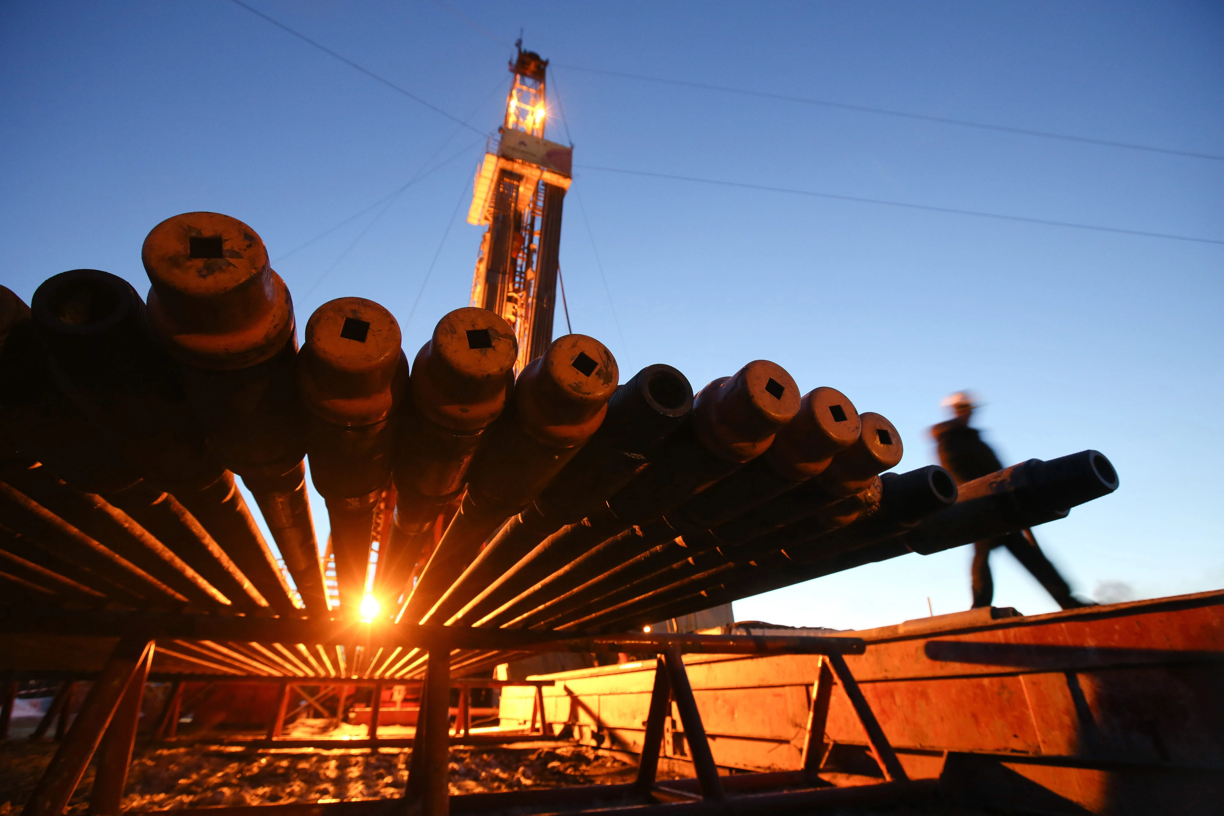 A worker passes an illuminated oil drilling rig and drill pipes in an oilfield