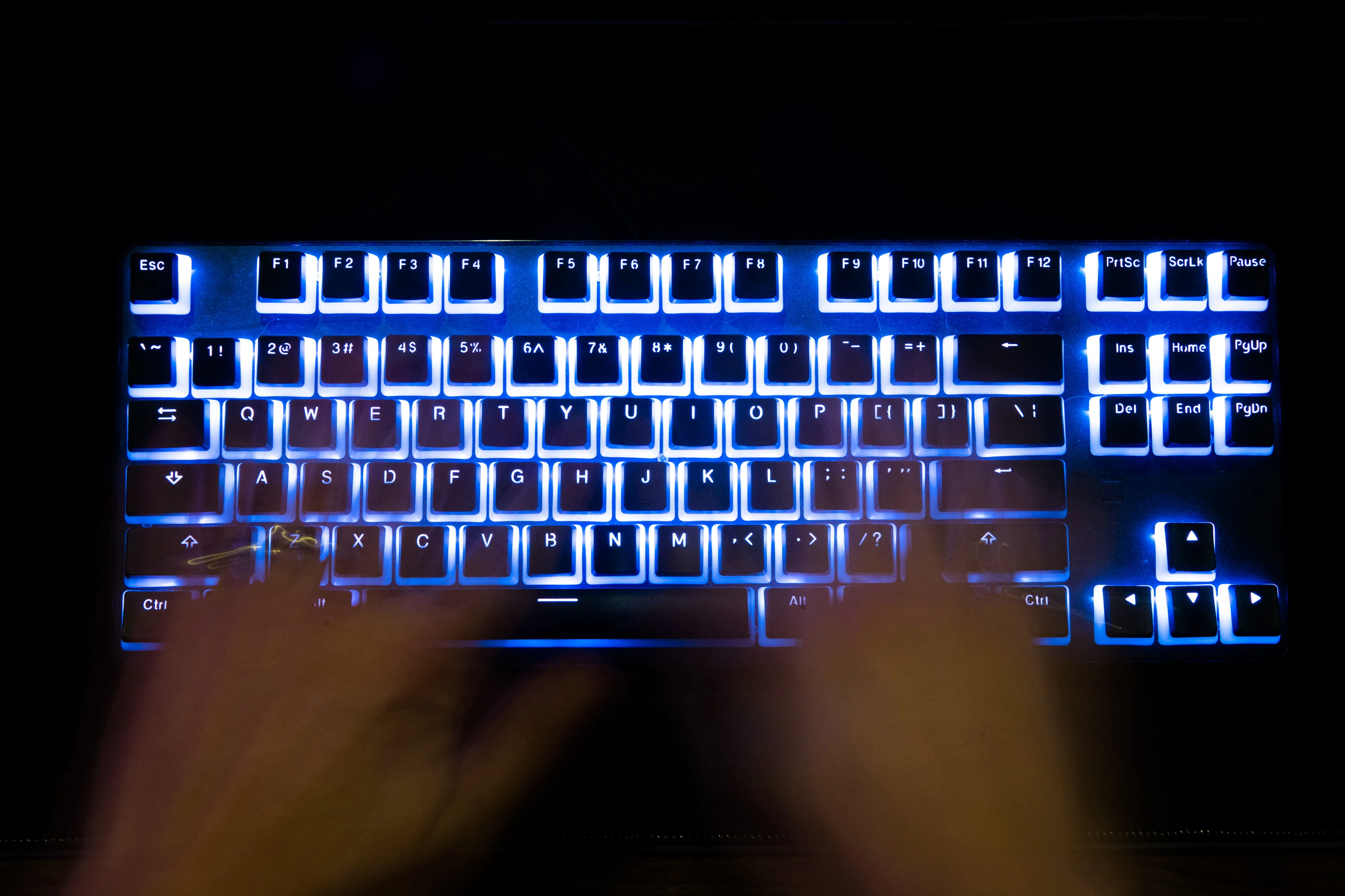 A man typing on a back lit computer keyboard.