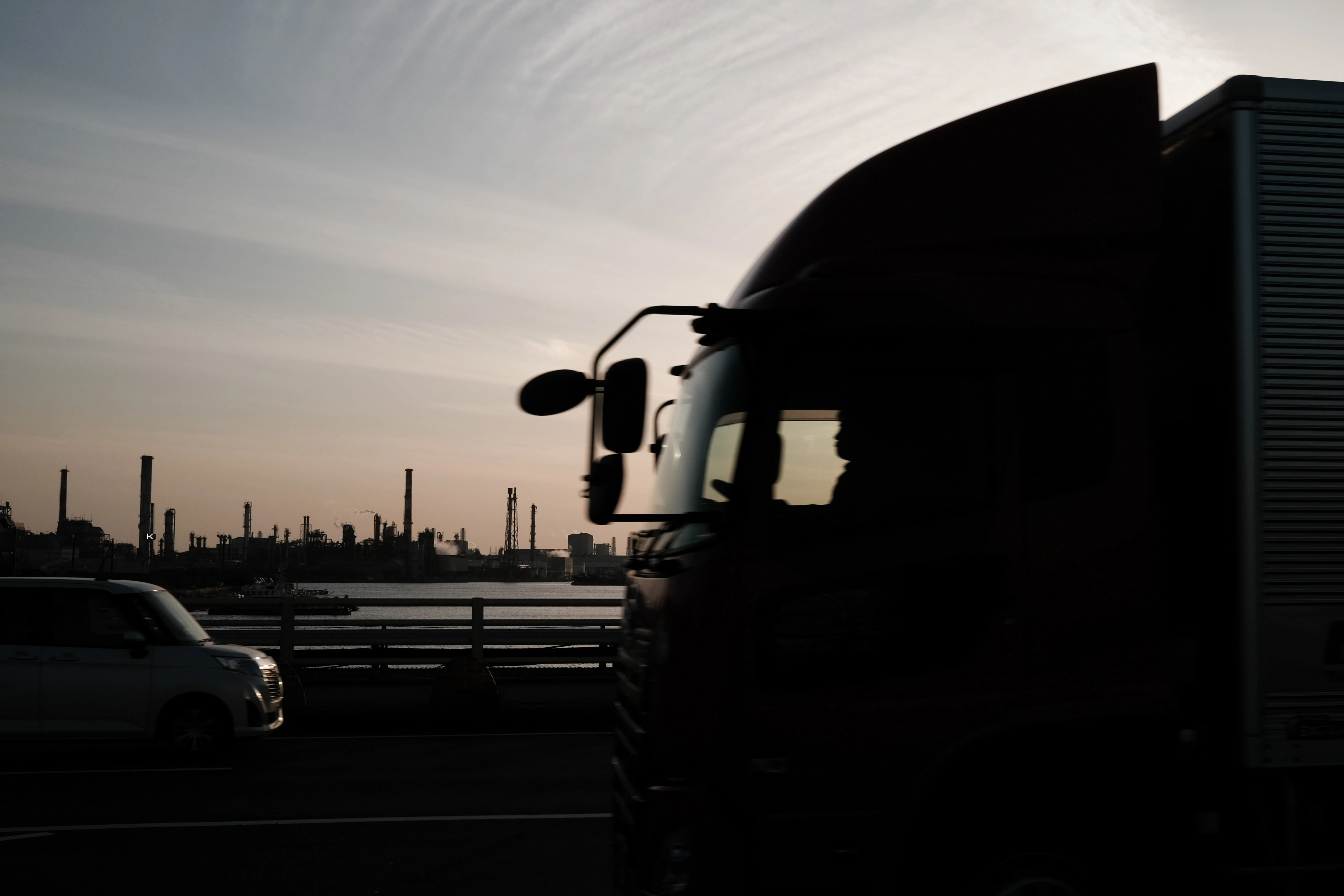 A heavy goods vehicle and car in silhouette on a highway