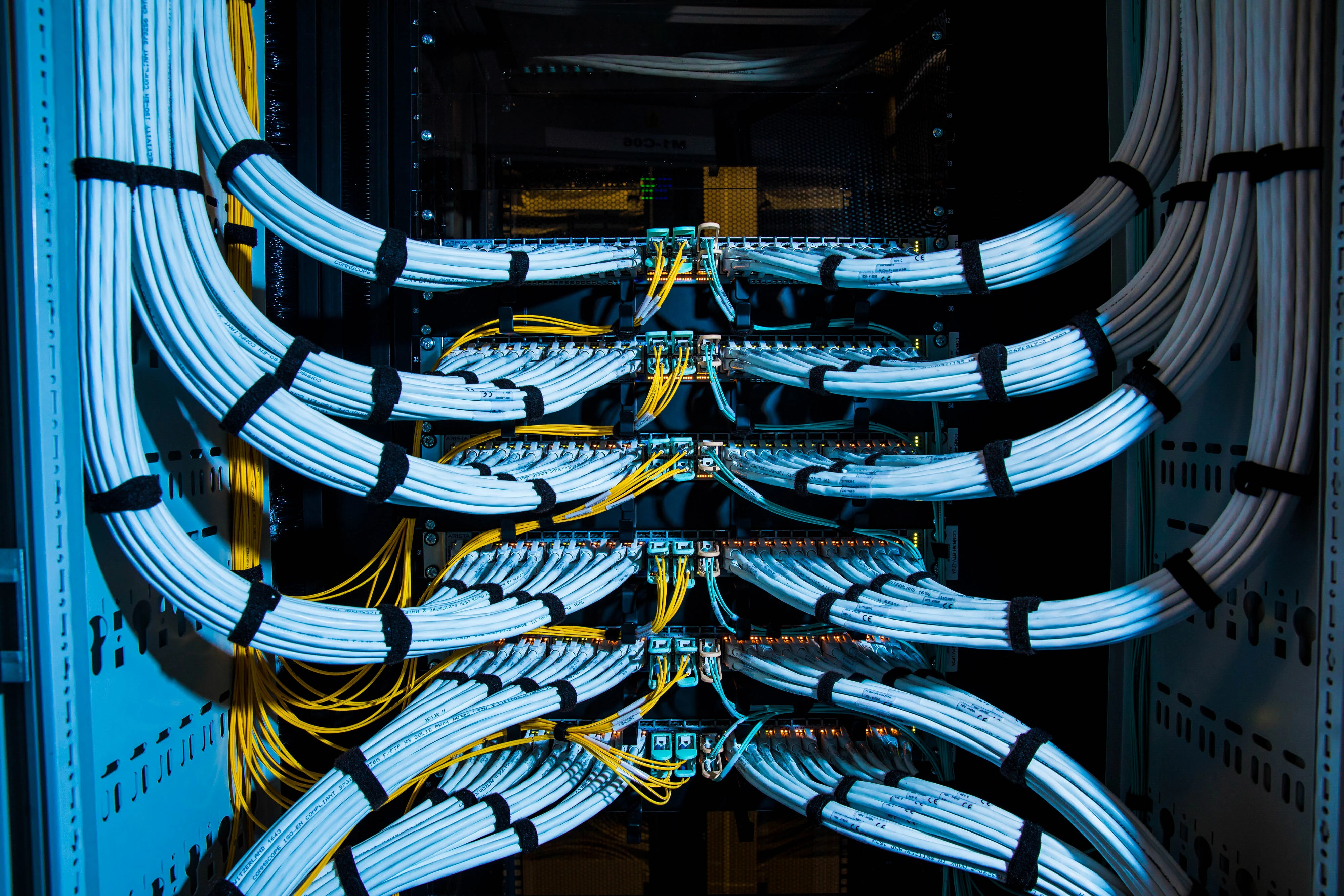 Fiber optic cables, center, and copper Ethernet cables feed into switches inside a communications room
