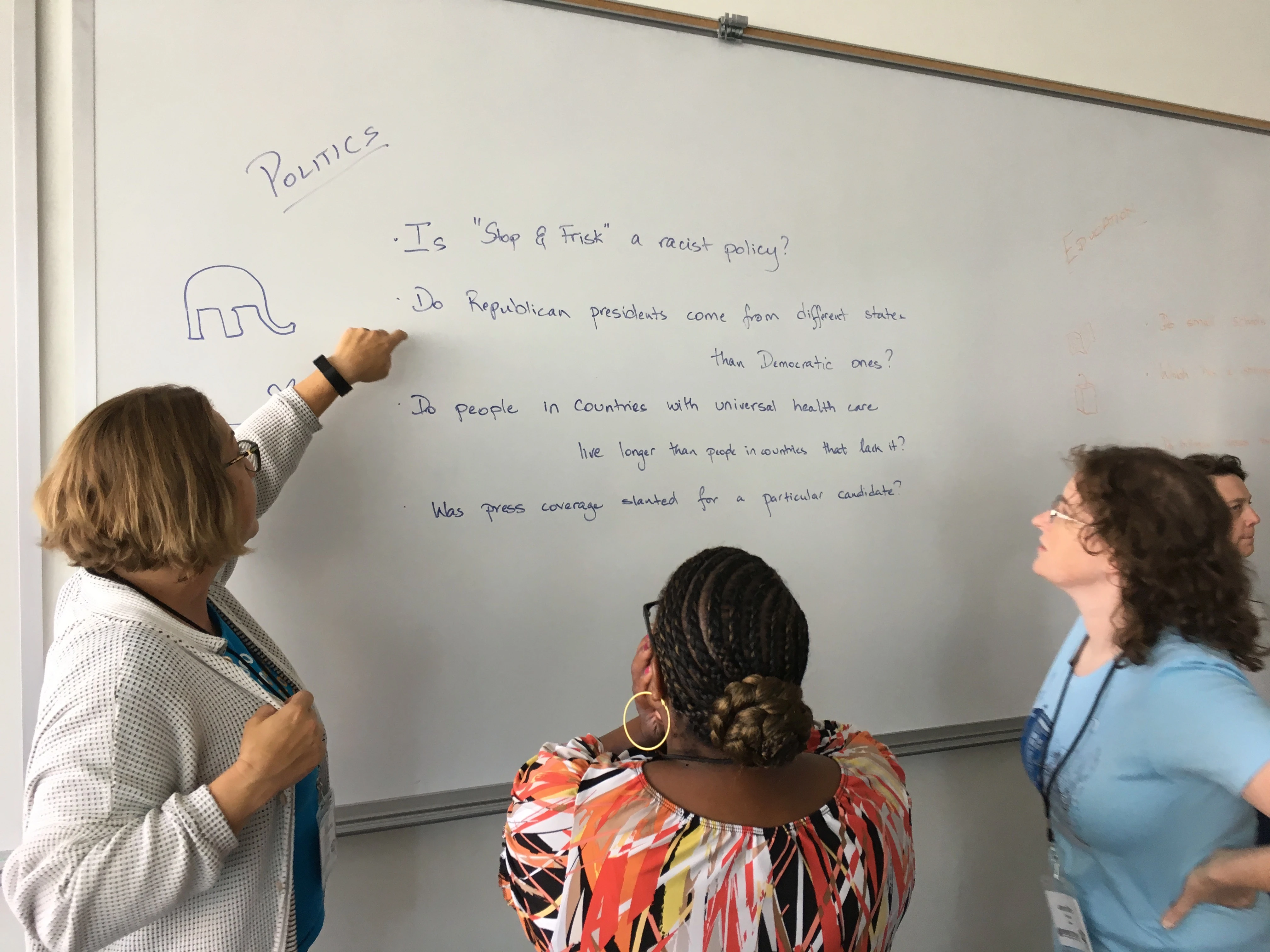 A woman mentor and two female students discuss data science points on a classroom whiteboard.