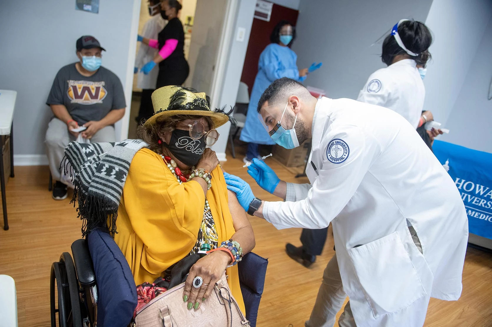 A doctor working at the Howard University vaccination center provides a vaccination to an elderly woman in a wheelchair.