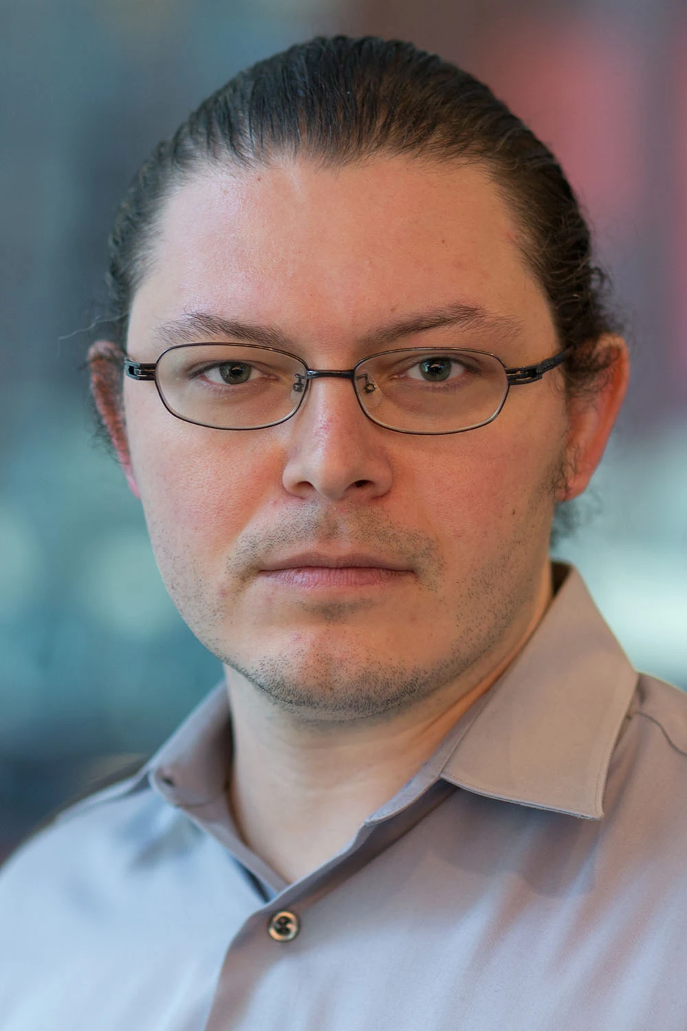 Gary Kazantsev poses for a headshot. He is a white male with thin-rimmed glasses, long hair pulled back, and wearing a gray collared shirt.