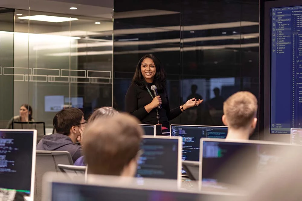 Bloombergs-120-Park-Office-early-careers-training A woman at Bloomberg's 120 Park New York office holds a microphone at the front of a classroom and trains a group of students on how to use the Bloomberg Terminal.